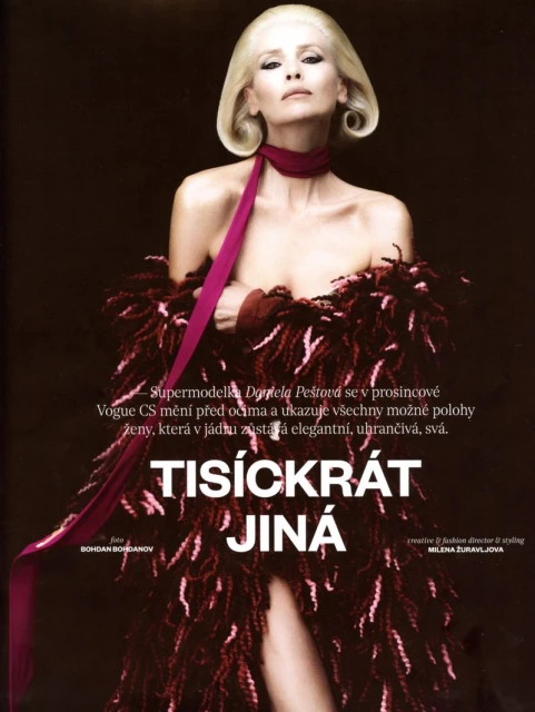 Fashion model in a feathered wrap with magenta ribbon poses indoors against a dark background in a beauty and fashion editorial.