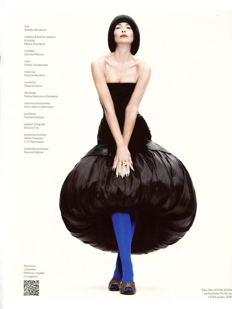 Elegant woman in a black strapless dress with blue tights poses in a studio setting, showcasing high fashion and unique style.