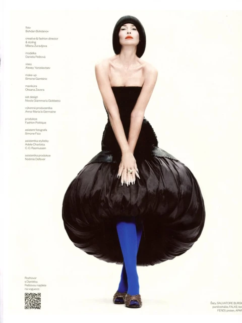 Elegant woman in a black strapless dress with blue tights poses in a studio setting, showcasing high fashion and unique style.