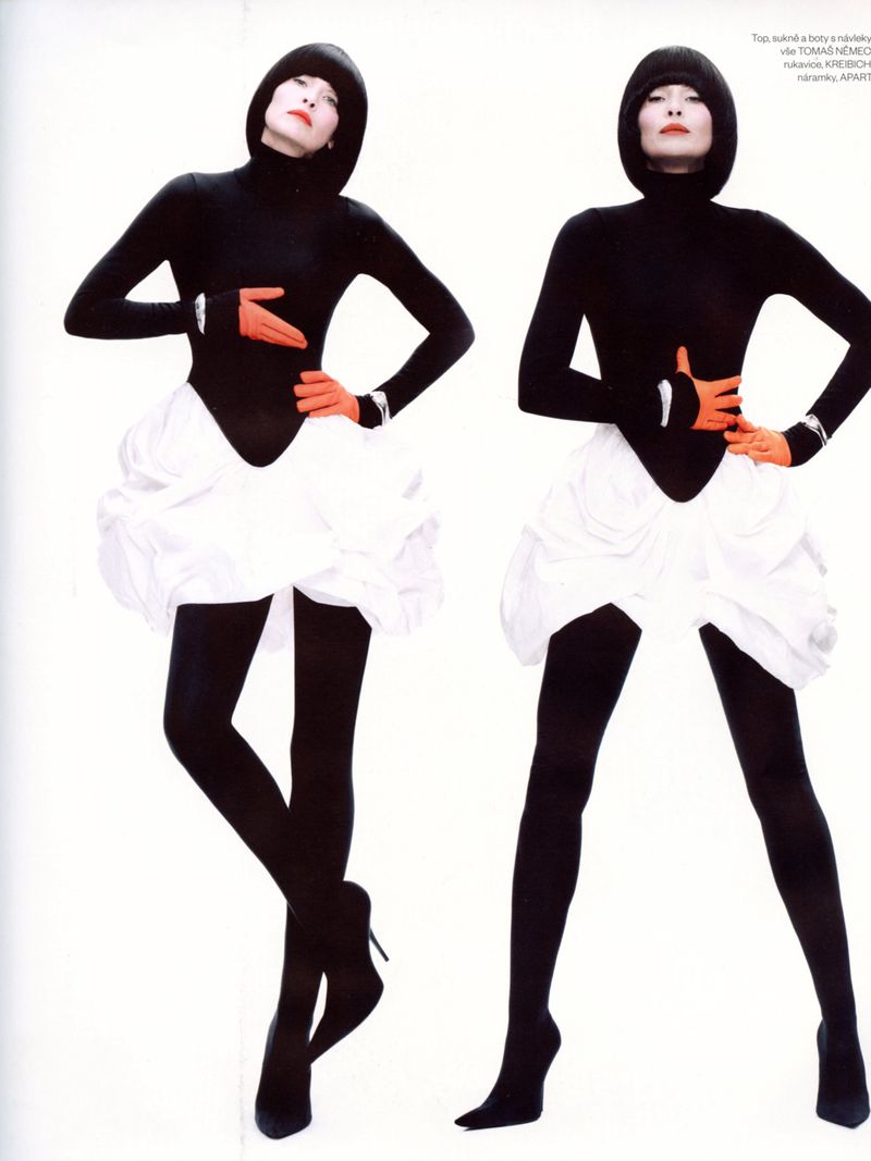 Two fashion models in black turtleneck leotards and black tights. The white ruffled skirts and orange gloves pop against a white backdrop.