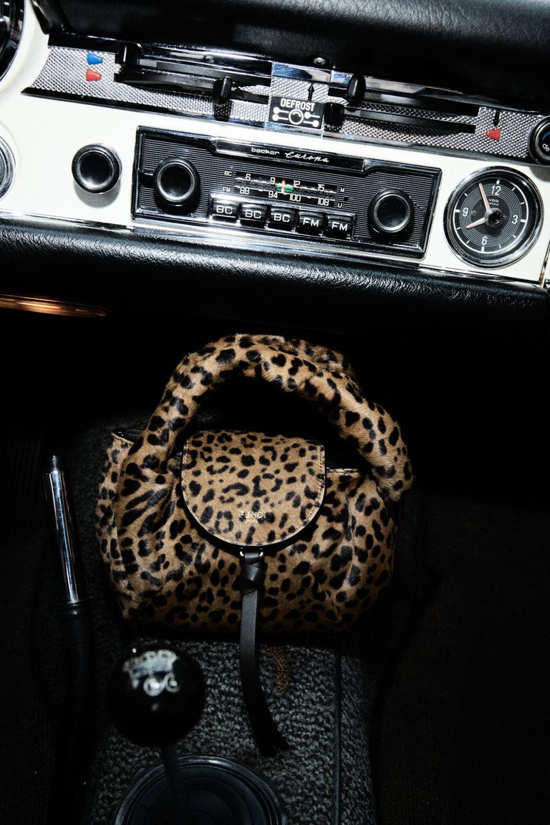 Leopard-print purse rests on the console of a classic car with a black gear shift knob and white vintage radio; interior shot.