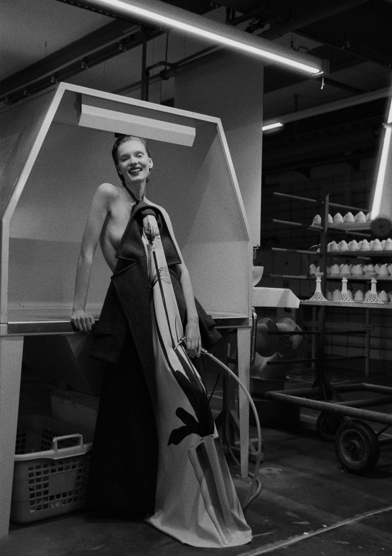 Striking black-and-white fashion shot of a woman in an industrial setting, wearing a draped garment with bold graphic elements.