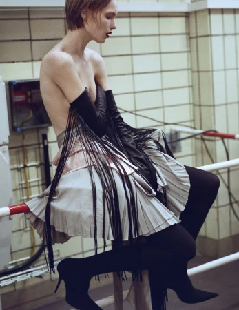 Side profile of a woman with short hair sitting on a railing with her legs crossed, wearing black tights and heels.