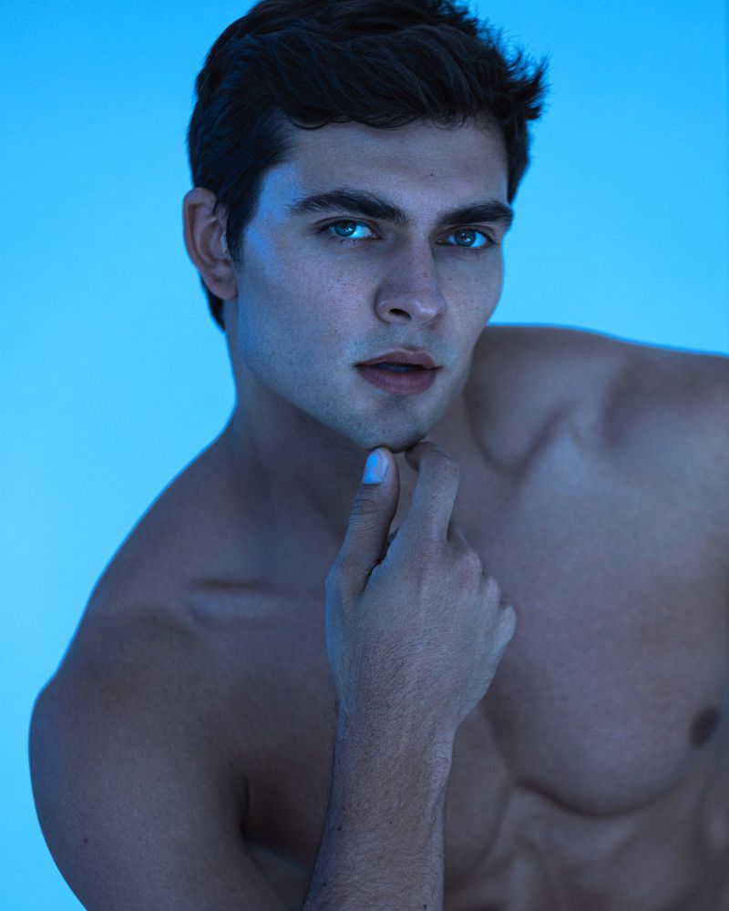 Striking close-up studio shot of a handsome adult male model with a thoughtful expression against a vibrant blue background.