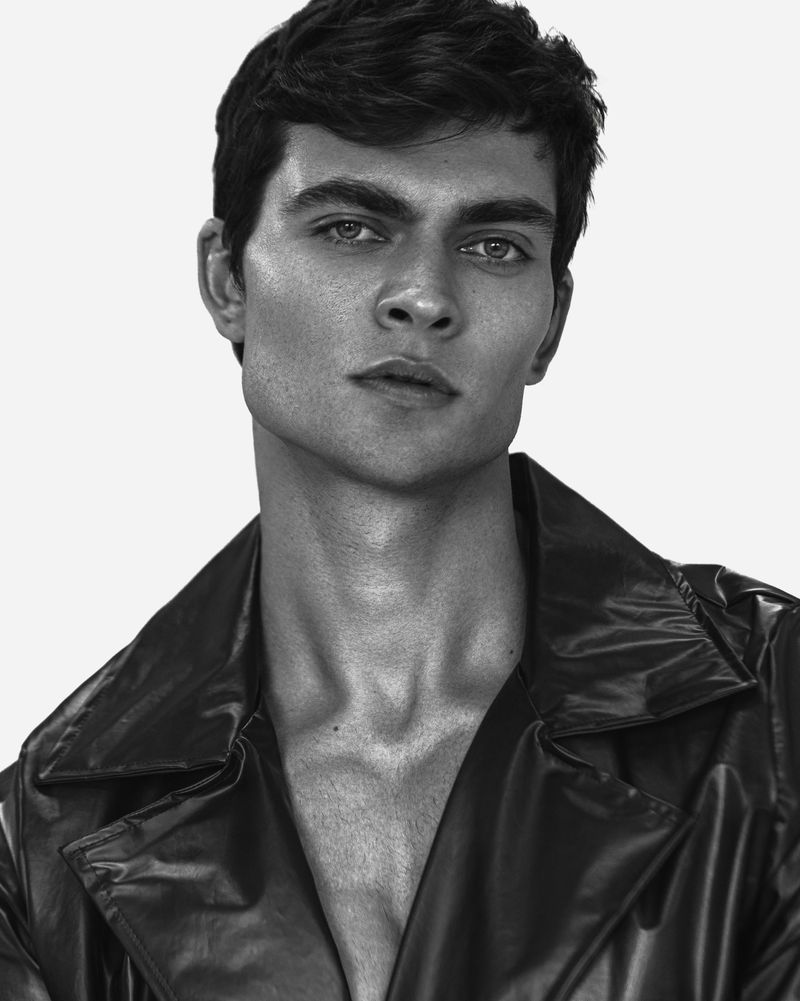 Monochrome portrait of a handsome male model wearing a dark leather jacket, looking intensely at the camera against a clean white background.