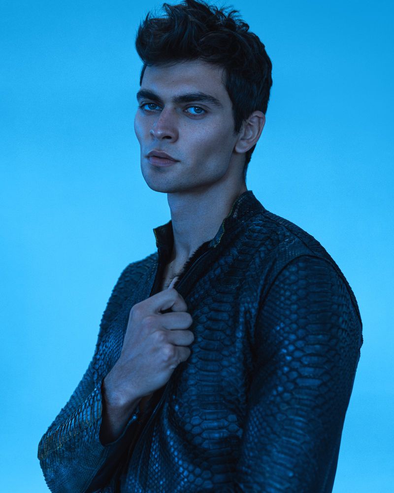Close-up portrait of model Kirill Kabachenko wearing a textured black jacket against a blue lit background.
