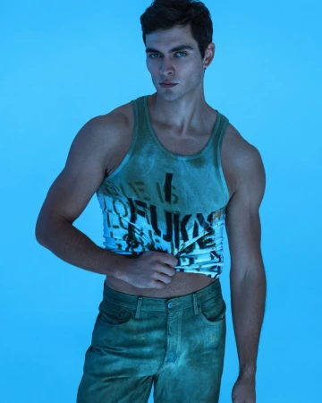 Model Kirill Kabachenko wearing a green printed tank top and green jeans against a blue background