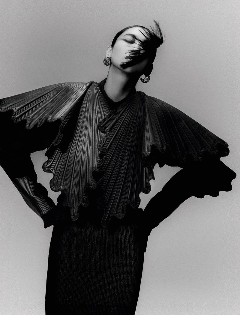 Monochromatic fashion shot of a stylish Asian woman wearing a distinctive black pleated top with voluminous sleeves and statement earrings.