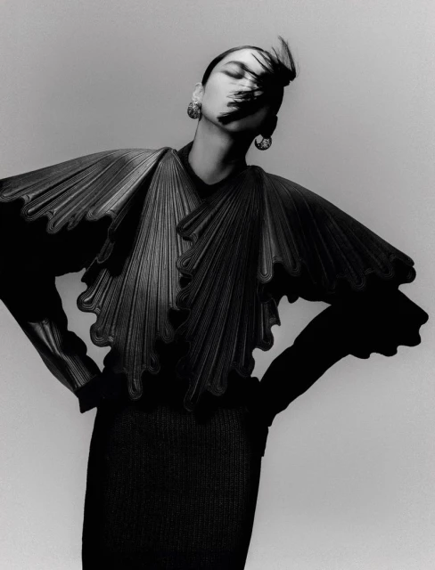 Monochromatic fashion shot of a stylish Asian woman wearing a distinctive black pleated top with voluminous sleeves and statement earrings.