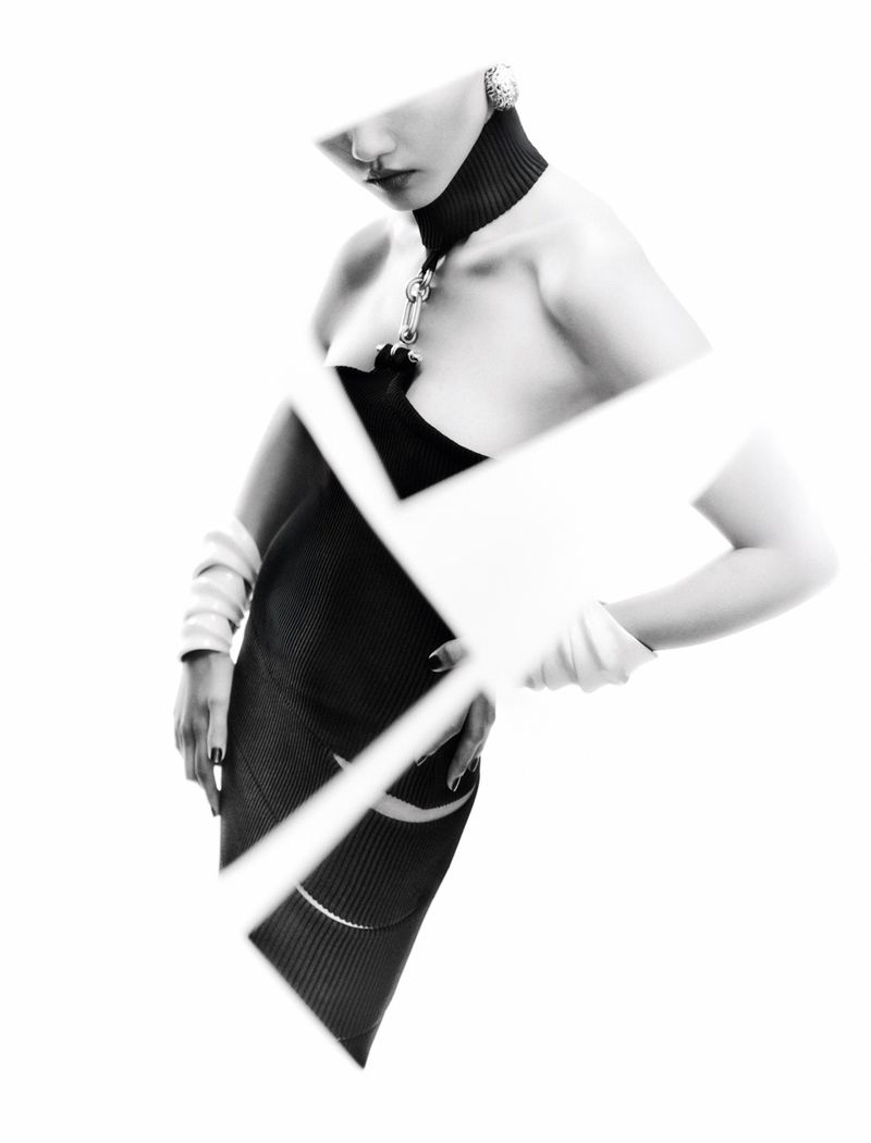 Fashionable adult female model in a black dress posing with hands on her waist against a white background with geometric shapes.