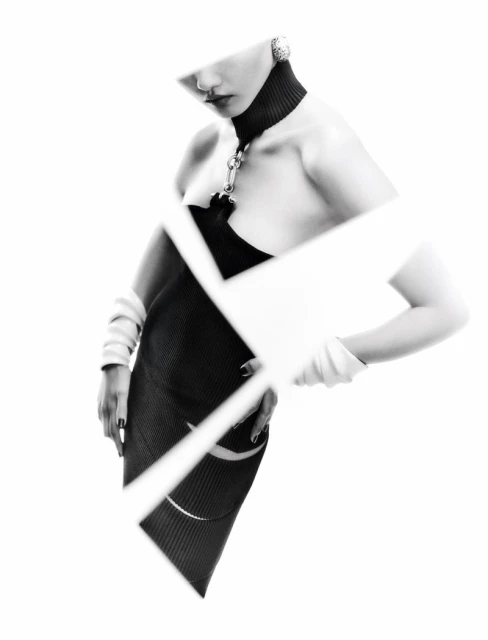 Fashionable adult female model in a black dress posing with hands on her waist against a white background with geometric shapes.