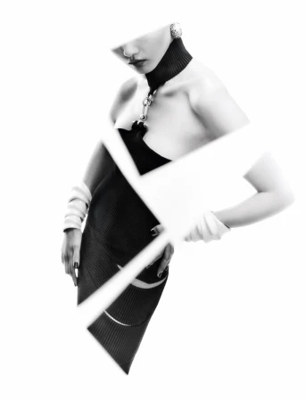 Fashionable adult female model in a black dress posing with hands on her waist against a white background with geometric shapes.