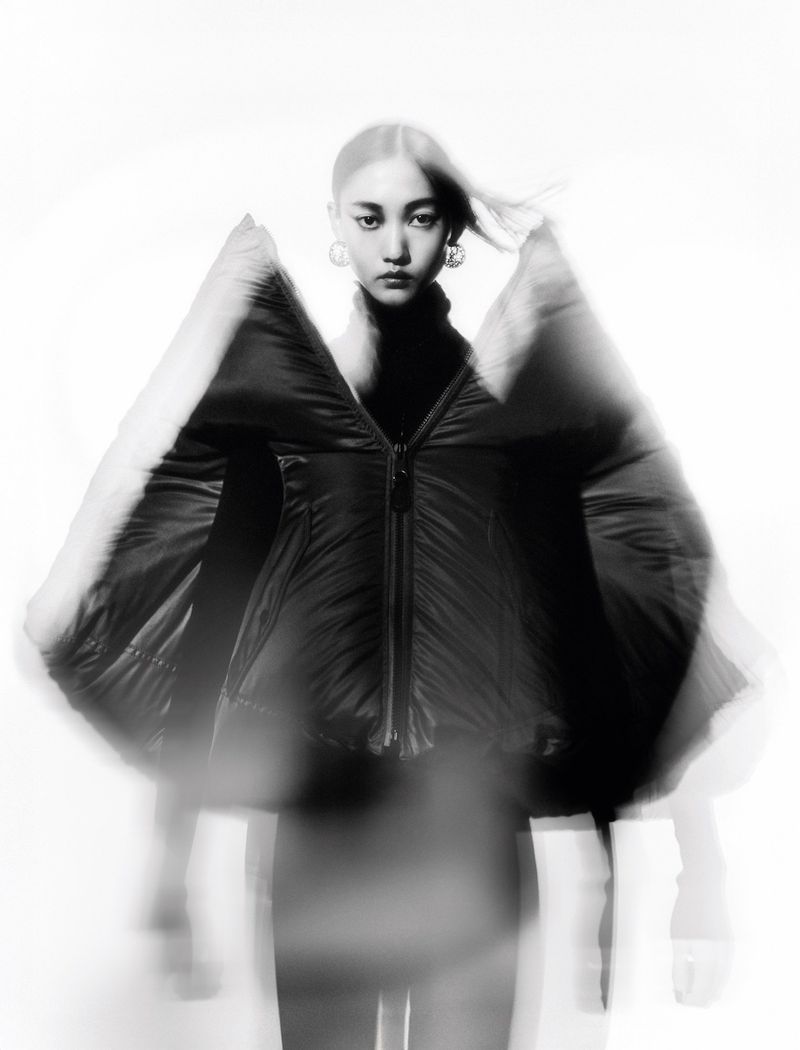 Asian woman in black puffer jacket poses against a white background with motion blur effect for fashion or beauty editorial content.