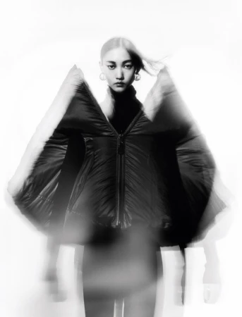 Asian woman in black puffer jacket poses against a white background with motion blur effect for fashion or beauty editorial content.