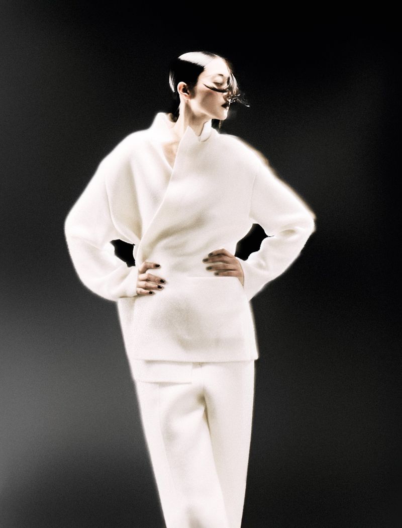 Fashion shot featuring a woman with dramatic eye makeup and a structured white outfit against a dark background in a studio setting.