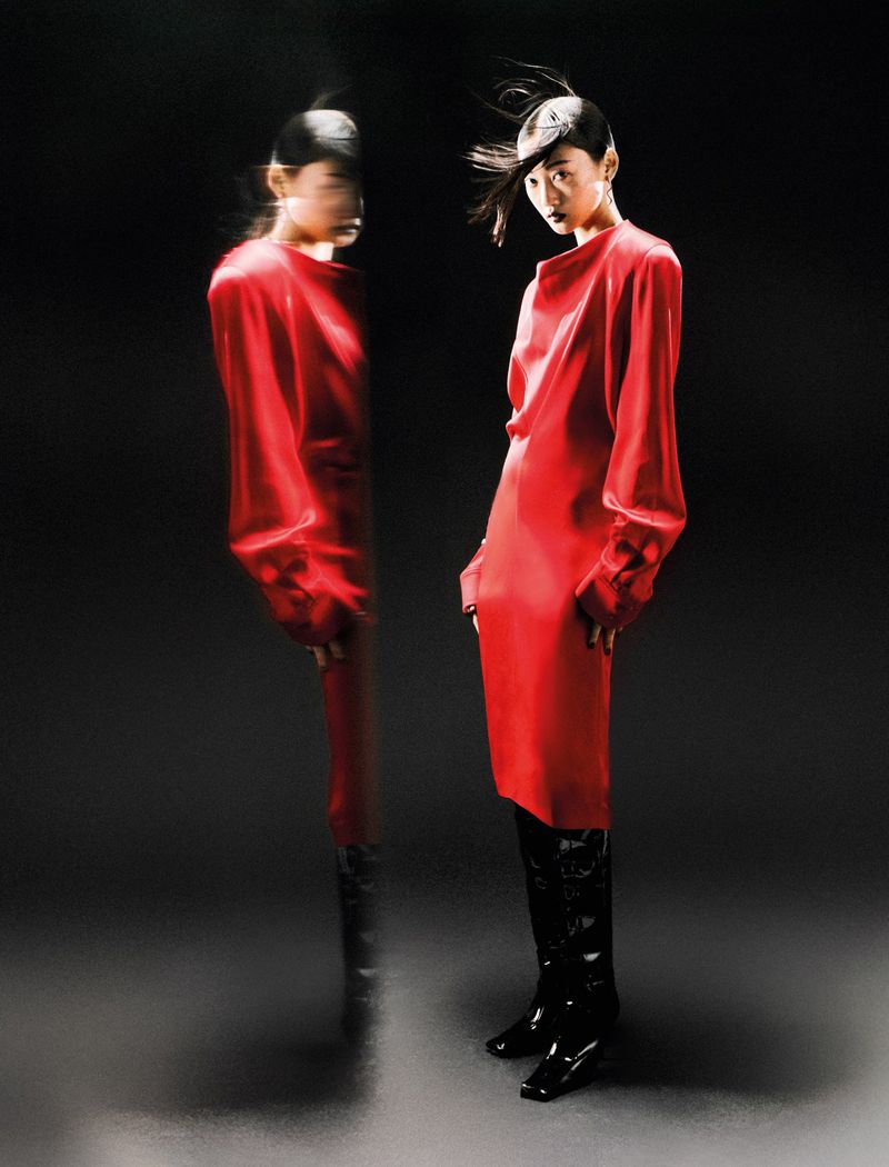 A fashion photo features an Asian woman in a red dress and black boots, standing against a dark backdrop with a blurred reflection.