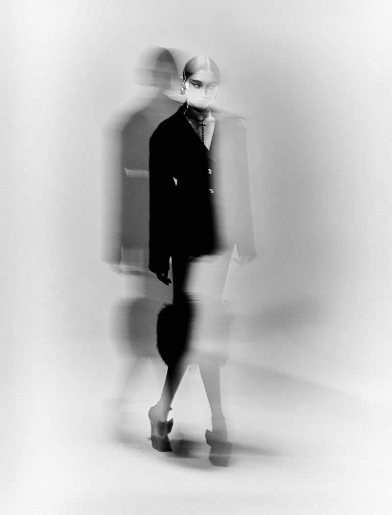 Monochrome fashion editorial of model Mona Kawasaki in a black tailored blazer and platform heels with motion blur.