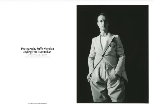 Editorial magazine spread showing a man wearing a sculpted light grey Walter Van Beirendonck suit against a dark background.
