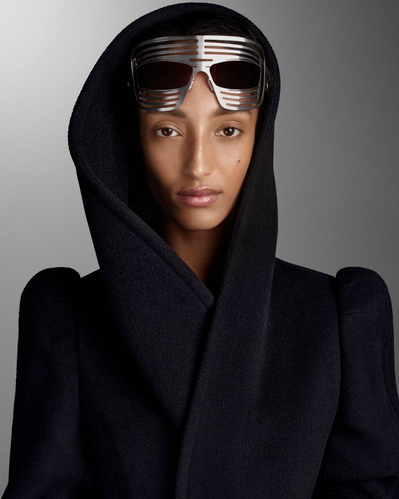 Mona Tougaard wearing a black hooded coat and futuristic silver slat sunglasses against a grey backdrop for D Repubblica