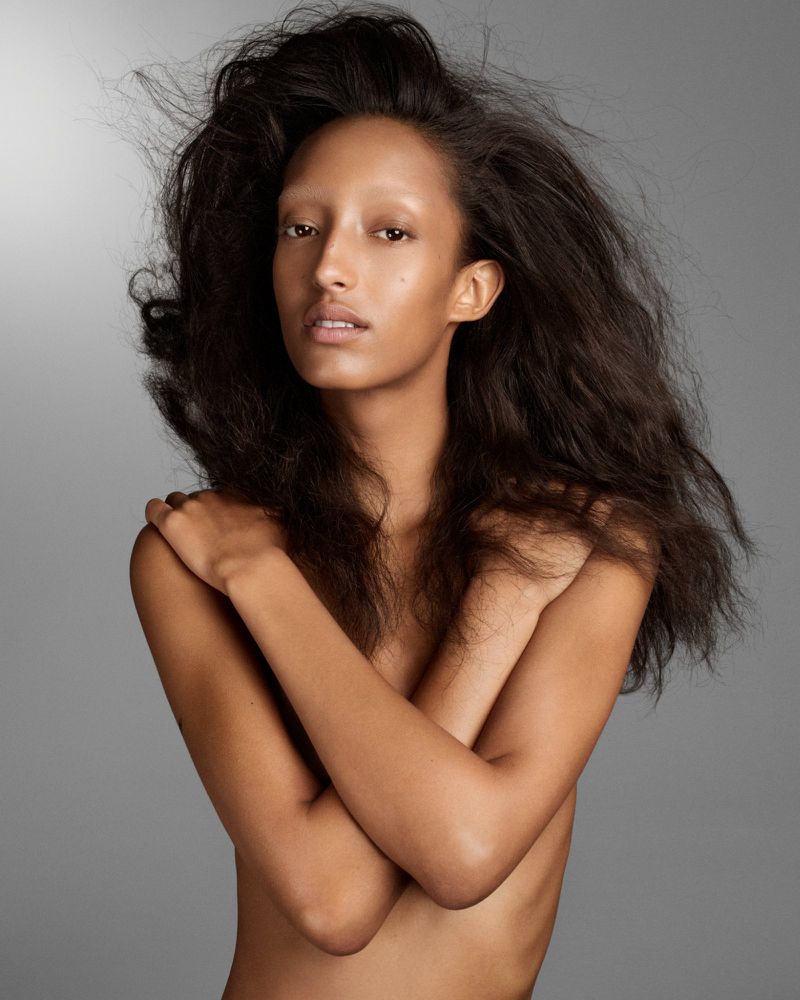 Striking studio portrait of a young adult female with dark hair, pale skin, and pale eyebrows against a neutral gray backdrop.
