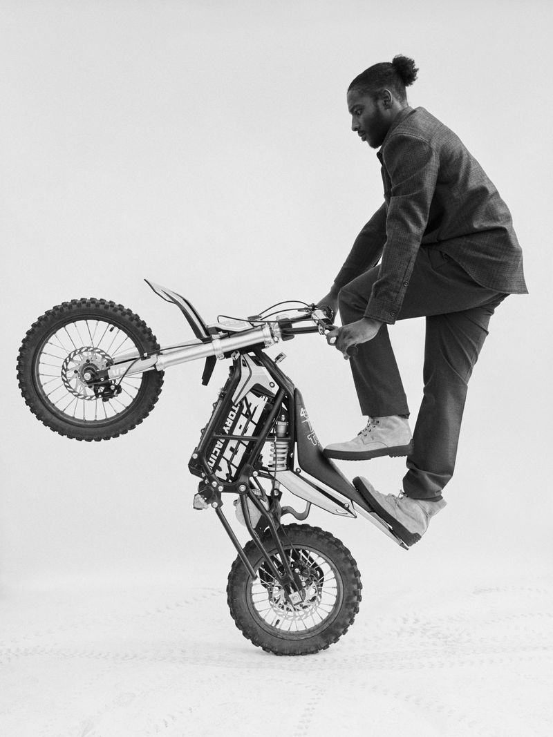 Monochrome shot of a man performing a wheelie on a dirt bike in a studio setting, captured with stark lighting and a focus on texture.