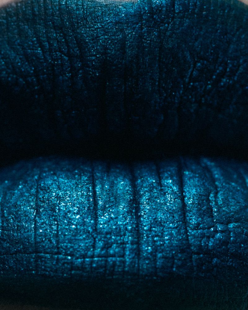 Close-up shot of a woman's lips covered in shimmering, metallic teal lipstick. The focus is on the texture and color of the makeup.