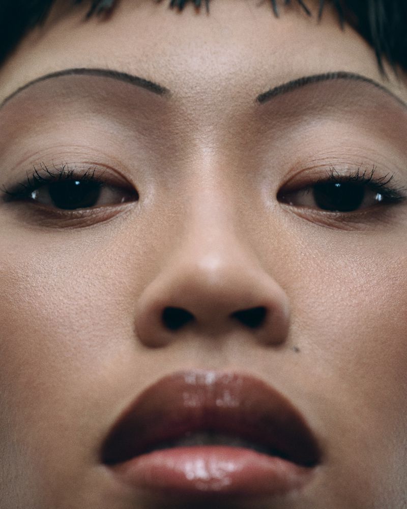 Close-up shot of an adult woman's face featuring dark eyes, fair skin, dark straight bangs, and glossy brown lips.