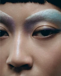 Close-up beauty portrait of a model featuring artistic purple eye makeup and bleached eyebrows for Tush Magazine.