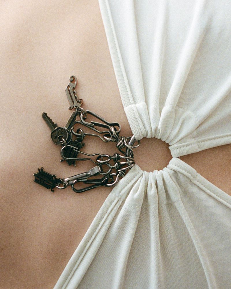 Close-up of a woman's chest wearing a white top with a ring detail, adorned with keys and chain for a fashionable and edgy look.