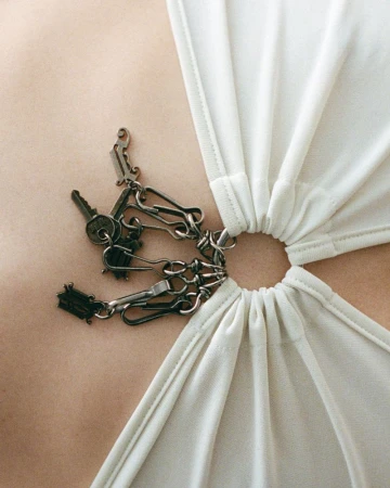 Close-up of a woman's chest wearing a white top with a ring detail, adorned with keys and chain for a fashionable and edgy look.