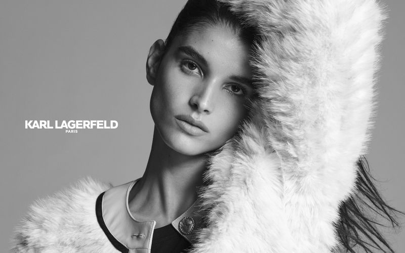 Close-up black and white fashion shot of a woman wearing a fur coat with Karl Lagerfeld Paris logo in the background, studio shot.