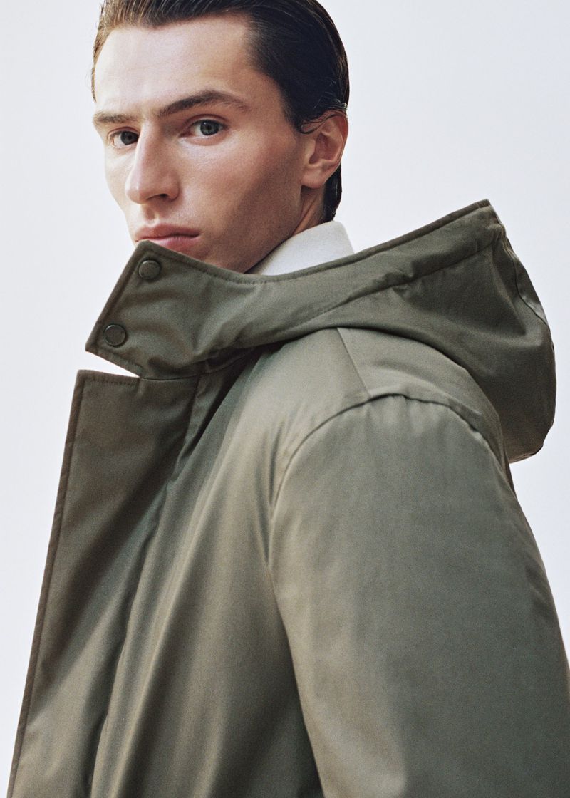 Clément Laguardia wearing an olive green hooded parka coat over a white collared shirt against a clean white backdrop.