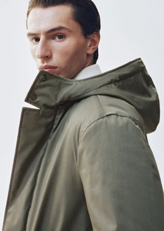 Clément Laguardia wearing an olive green hooded parka coat over a white collared shirt against a clean white backdrop.