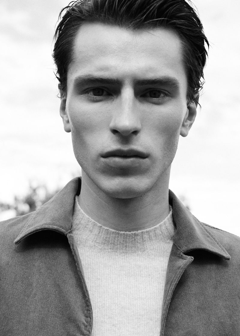 Black and white close-up portrait of model Clement Laguardia wearing a collared jacket and knit sweater.