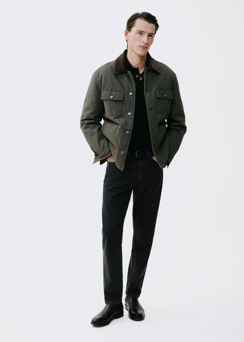 Full-length shot of a handsome adult male model wearing a collared shirt, dark jeans, and a jacket in a white photo studio setting.