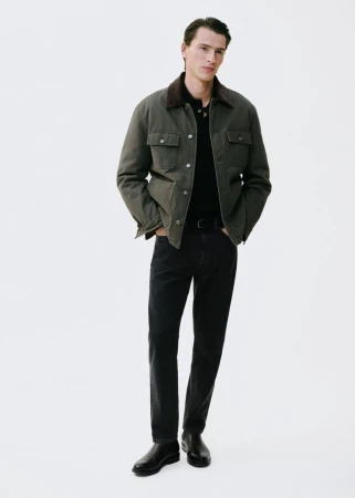 Full-length shot of a handsome adult male model wearing a collared shirt, dark jeans, and a jacket in a white photo studio setting.