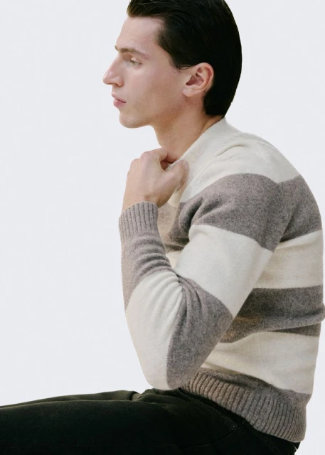Side profile studio shot of an adult male in a striped sweater against a white background, showcasing fashion and simplicity.