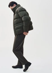 Man wearing a dark green puffer jacket and dark trousers against a white seamless background