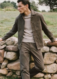 Model leaning against a low stone wall wearing an olive jacket and matching trousers for Mango Man