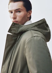 Clément Laguardia wearing an olive green hooded parka coat over a white collared shirt against a clean white backdrop.