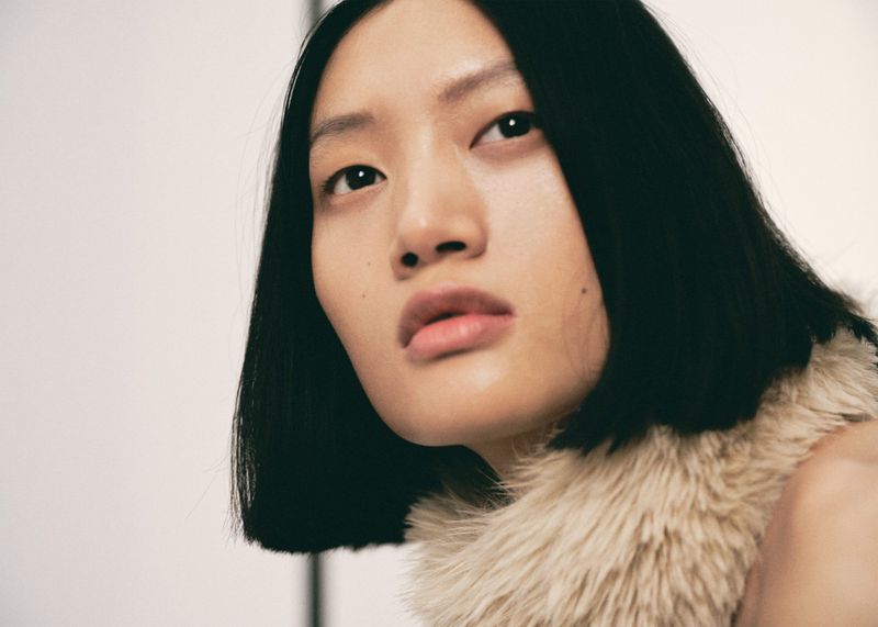 Close-up portrait of an Asian adult female with short black hair, wearing a fuzzy beige collar against a light neutral background.