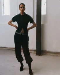 Model Suzie Bird poses with hands on hips wearing a black short-sleeved shirt and cropped trousers for Renaissance Renaissance S/S 26.