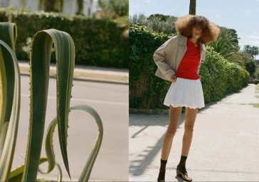 Model with voluminous curly hair in a red top, beige jacket, and white mini skirt standing on a sidewalk near agave plants.