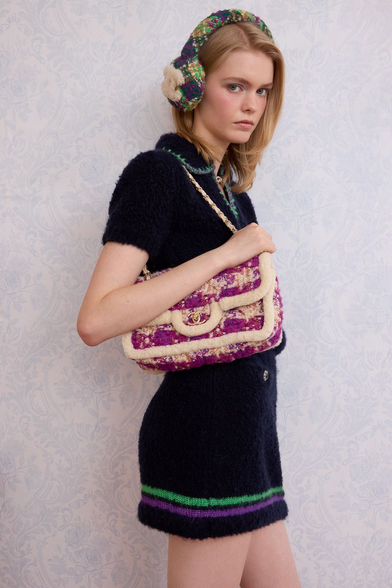 Woman wearing a dark blue skirt and top with matching floral-print headphones, carrying a cream and pink tweed handbag.