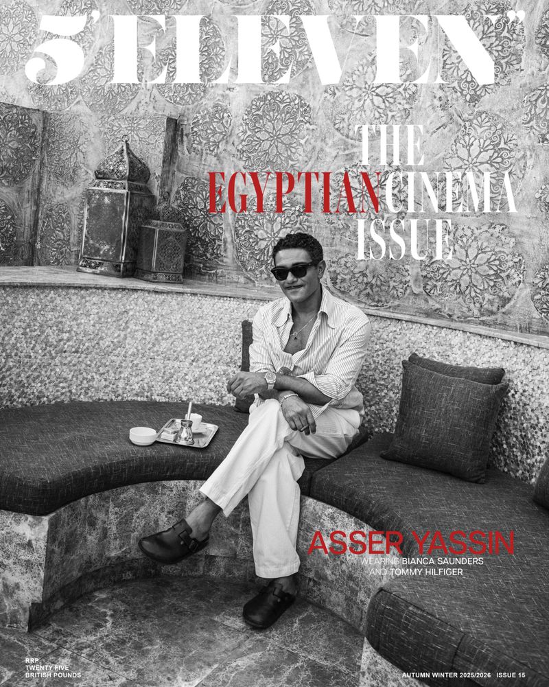 Magazine cover featuring a seated man in sunglasses wearing a white shirt and pants, accessorized with a watch, in black and white with red text.