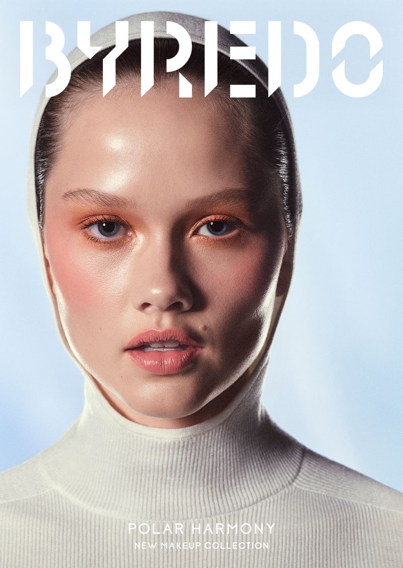Close-up shot of a fair-skinned young woman with orange makeup and a white turtleneck, modeling for a Byredo makeup collection ad.
