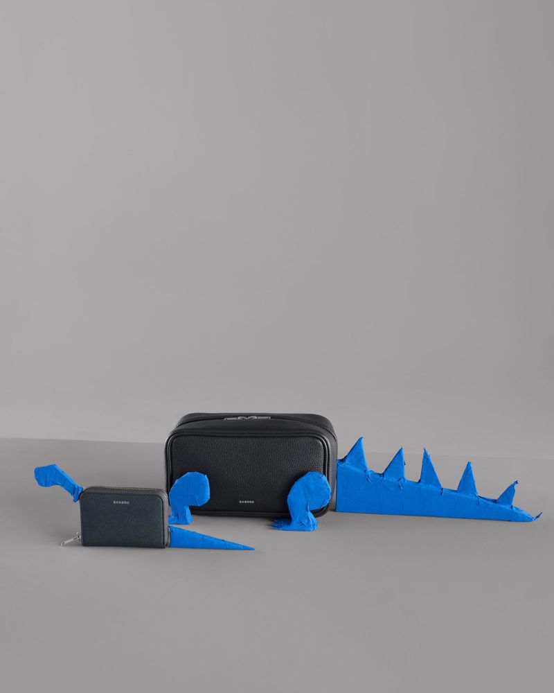 Arrangement of a small and a large cosmetic bag, with a blue paper dinosaur cutout on a grey backdrop, studio shot, minimal style.