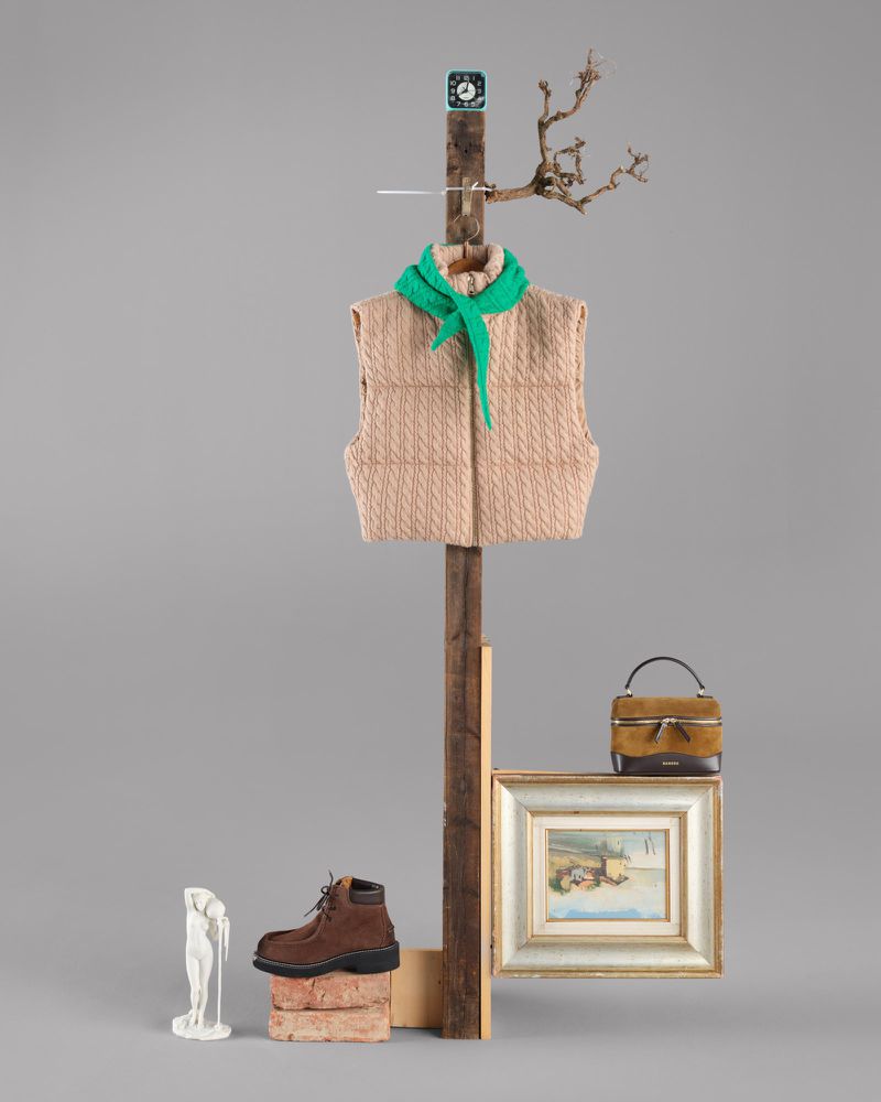 Still life composition with vest, scarf, boot, and artwork against a gray background. Creative fashion and art object arrangement.