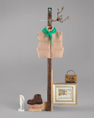 Still life composition with vest, scarf, boot, and artwork against a gray background. Creative fashion and art object arrangement.