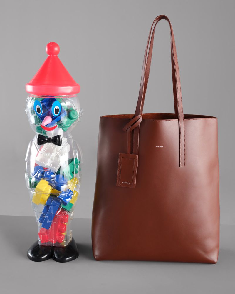 Brown leather tote bag with a plastic toy figure filled with blocks on a grey surface, studio shot.